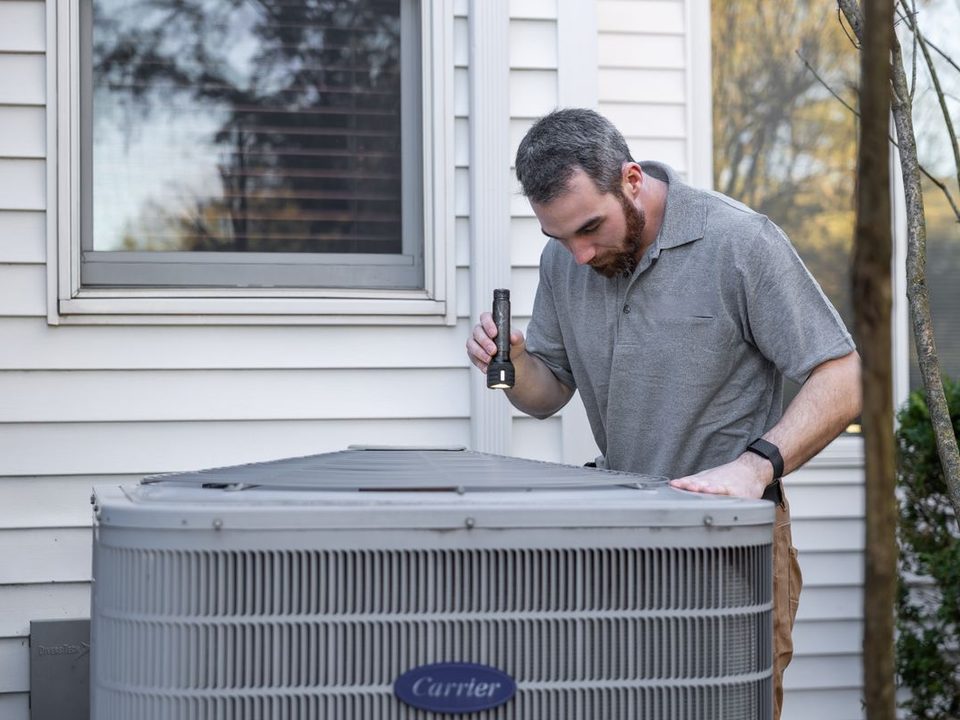 Technician inspecting a central air condenser beside a house